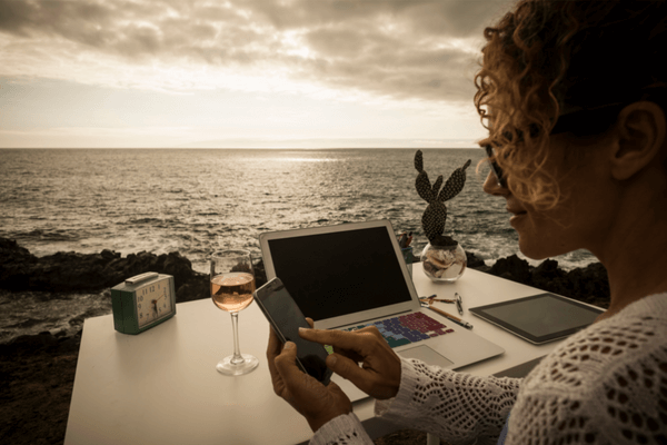 여자가-석양이지는-바닷가카페에서-노트북과-와인이있는-테이블에서-휴대폰을-보고있는-모습