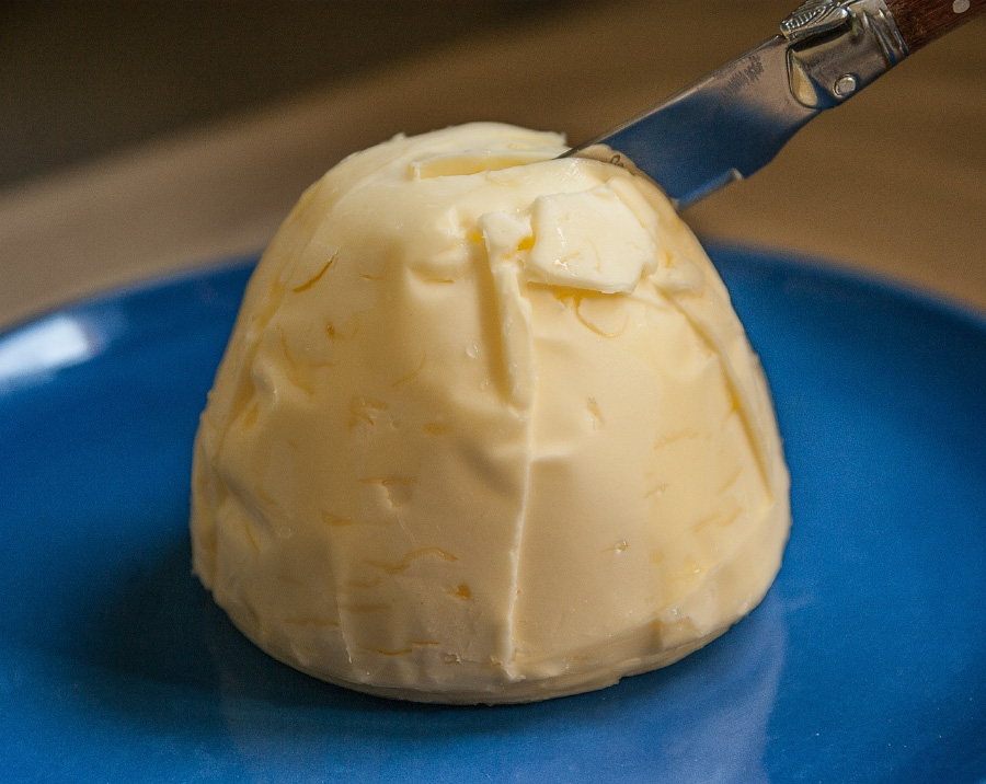버터를 동그랗고 파란 접시 위에 한덩이 놓고 칼로 버터를 반으로 자르는 것을 확대하여 찍은 사진
