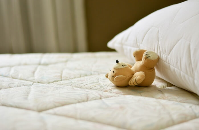 침대 매트리스 위에 있는 작은 곰돌이 인형