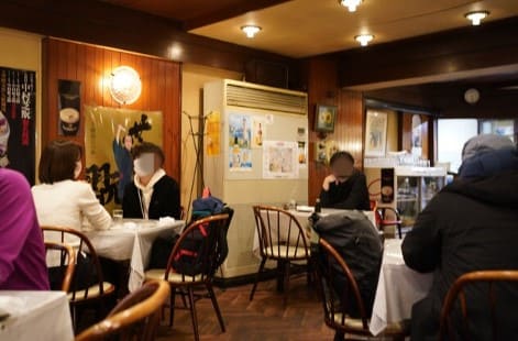 갈색나무를 위주로 한 식당 실내 사진 사람들이 동그란 테이블 앞에 앉아있다.