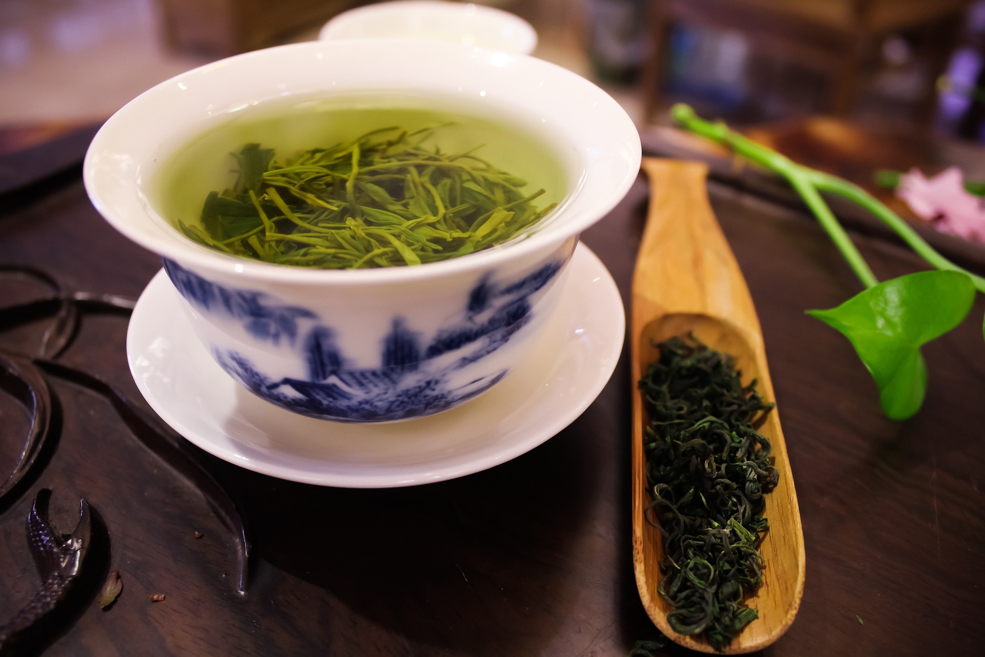 green-tea-3528474_1920 고동색의 티테이블 위에 하얀색 찻잔을 놓고 그 속에 신선한 녹차잎과 뜨거운 물을 붓고, 녹차를 우려내고 있고 그 옆에는 녹차잎을 가득 담은 나무 숟가락이 있는 사진