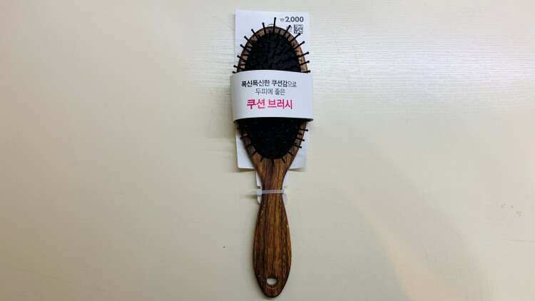 갈색 손잡이와 몸통으로 이뤄진 헤어 쿠션 브러시