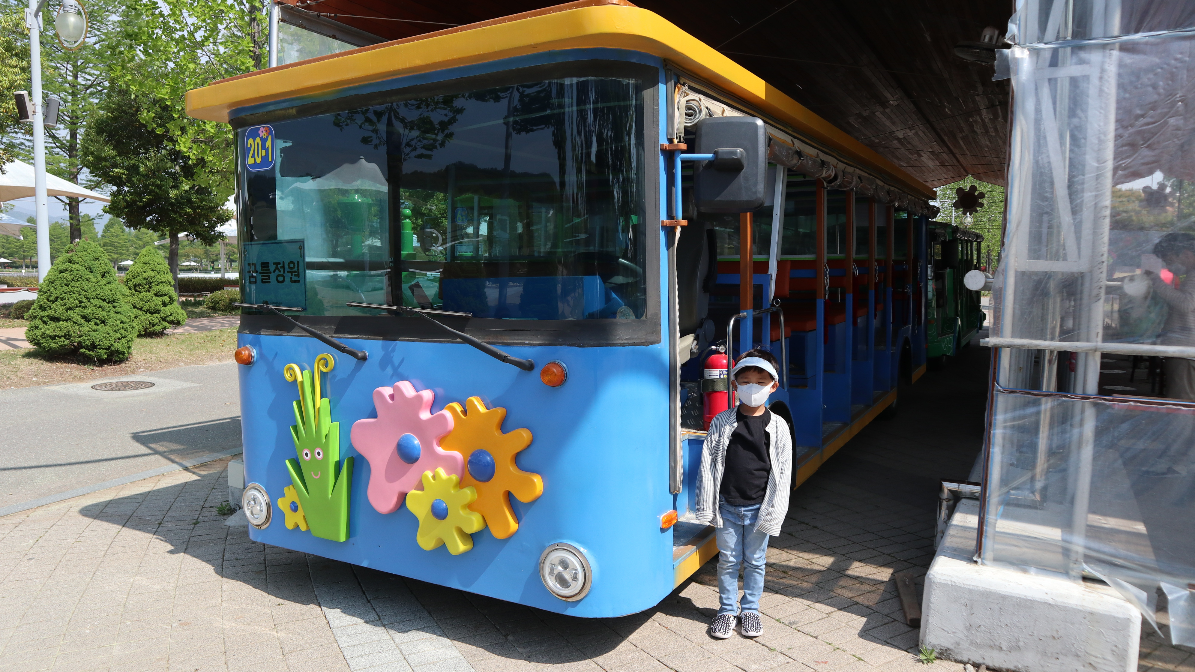 파란색 버스에 풀과 꽃무늬가 있고 옆에 한 아이가 서있다