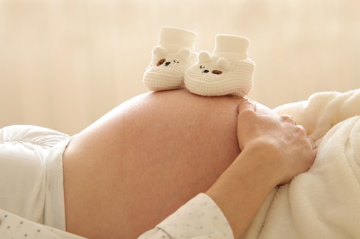 누워있는 임산부 배 위에 아기신발이 올려져 있는 사진