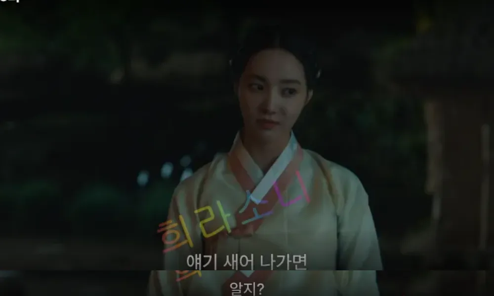 어두운 밤&amp;#44; 흰색 한복을 입은 미령이 약간 비웃는 듯한 표정을 짓고 있다. 배경은 어둡고 나무와 흐릿한 불빛이 보인다. 자막은 