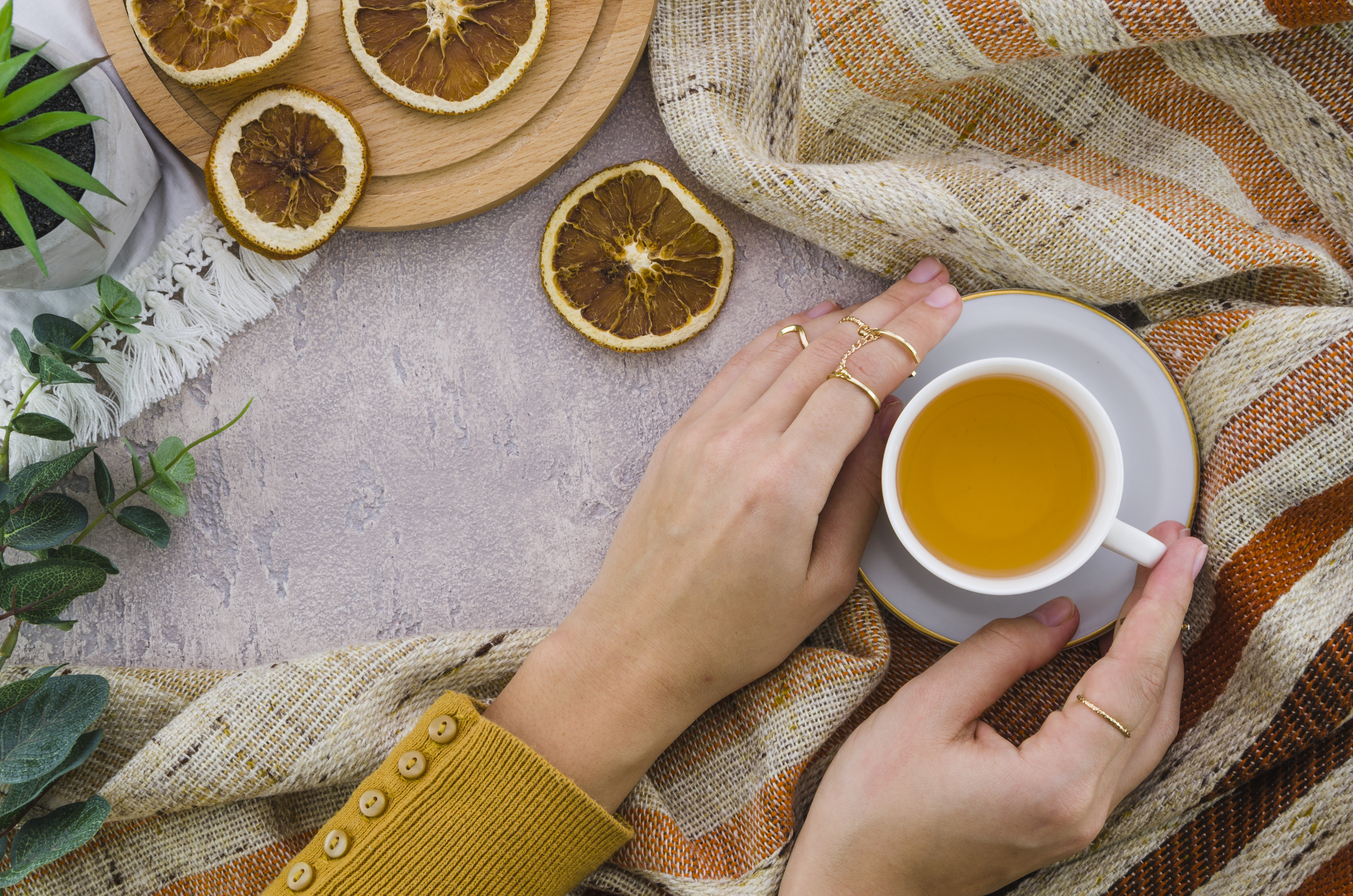 overhead-view-woman-s-hand-holding-herbal-tea-cup-dried-lemon-textured-backdrop