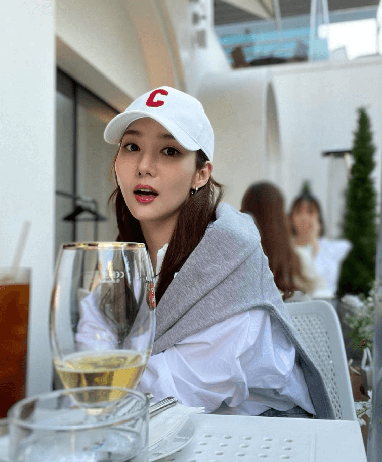 박민영이 하얀색 야구 모자를 쓰고 카페 야외 테라스에 앉아있다.