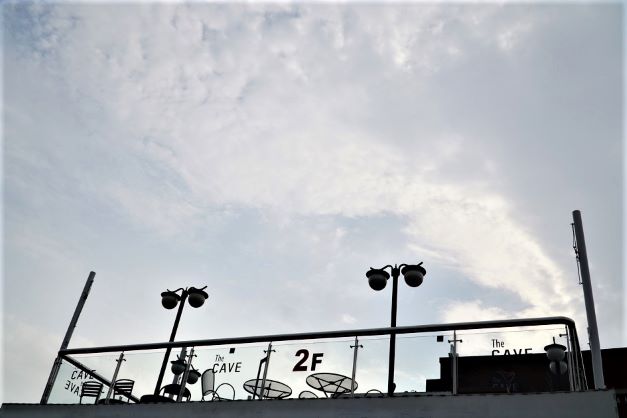카페 2층 테라스 위 구름낀 흐린 하늘&#44; 올려다 본 사진&#44; 테라스에 원형 철제 테이블과 의자. 은방울꽃 모양의 보안등&#44;