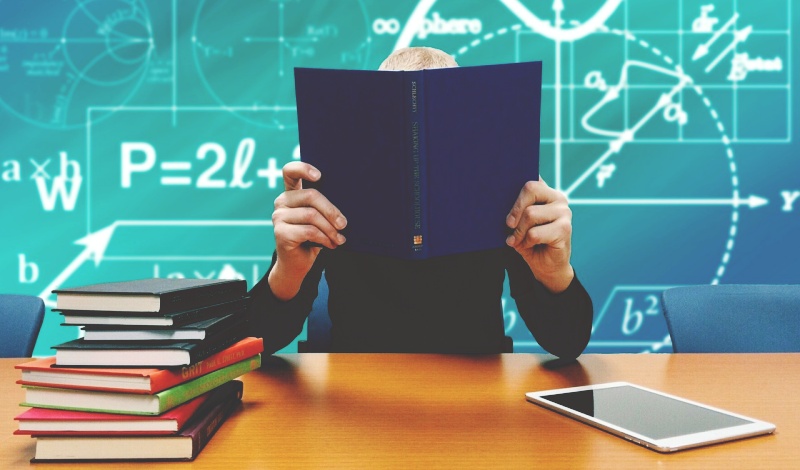 A student studying with textbooks and a tablet, possibly comparing dormitory and homestay options in a U.S. academic environment