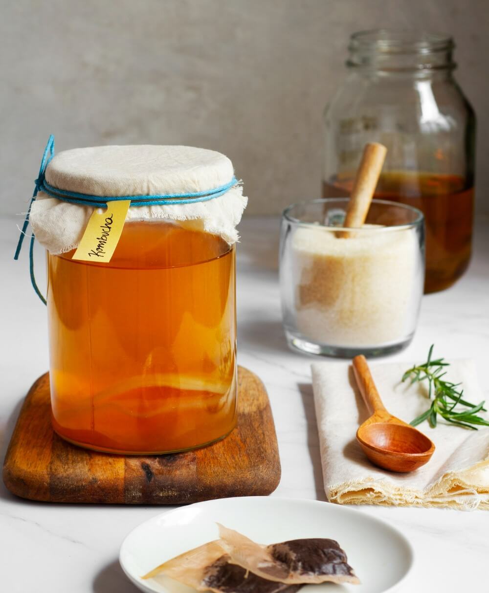 유리병에 꿀이 들어있고 그 주위로 나무 숫가락과 요리 재료들이 놓여져 있다.