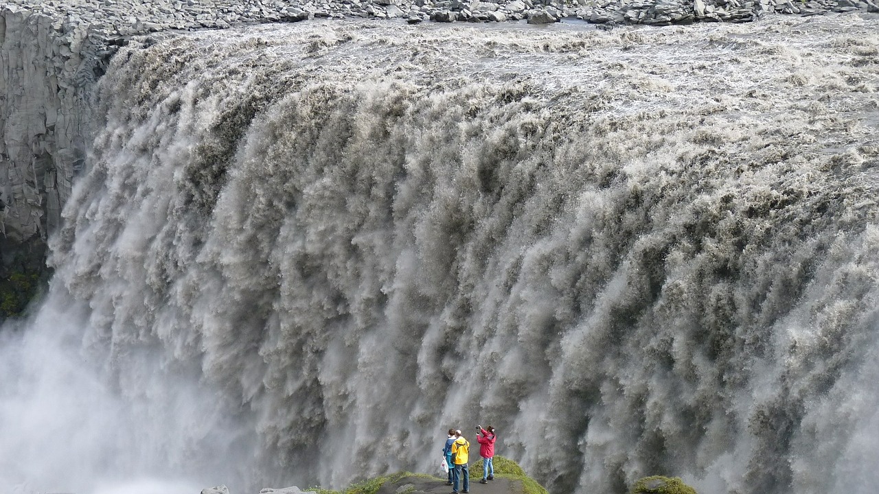 엄청난 양의 물이 떨어지는 아이슬란드 북부의 데티포스에서 사진을 찍는 세 명의 사람들