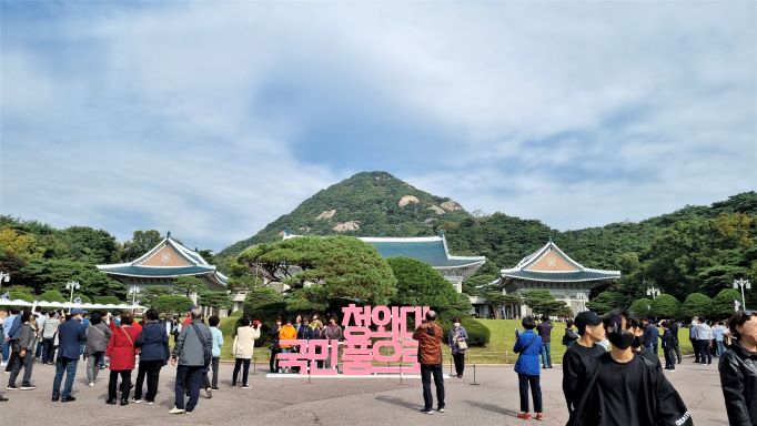 본관 앞 청와대 국민품으로 라는 큰 글자를 분홍색으로 만들어 세워 놓았고&#44; 청와대 뒤는 세모로 우뚝 솟아 있는 북악산&#44; 수많은 관람객들&#44;