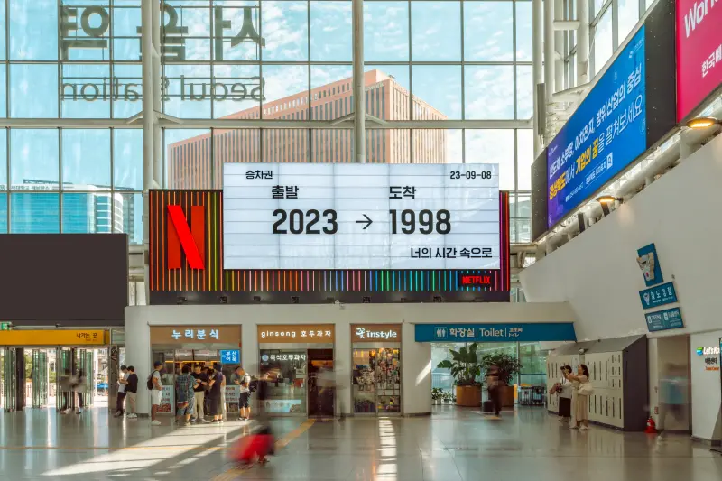 서울역 실내 상점 입구 벽면의 전광판에 2023년 출발과 1998년 도착으로 표시된 너의 시간속으로 광고