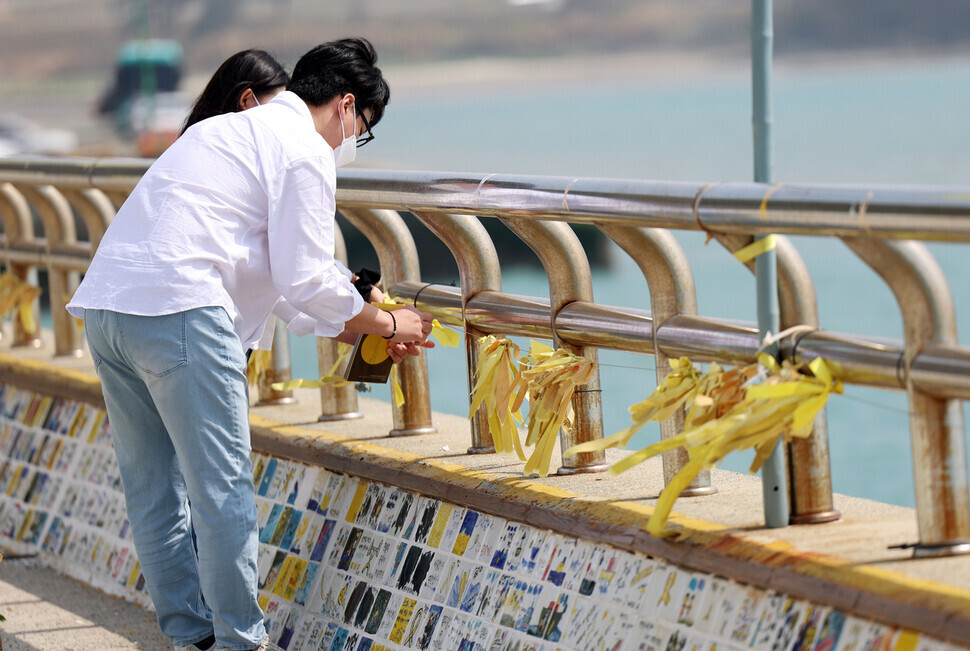 세월호 참사 9주기인 16일 전남 진도군 팽목항 방파제에서 한 추모객이 노란 리본을 묶고 있다