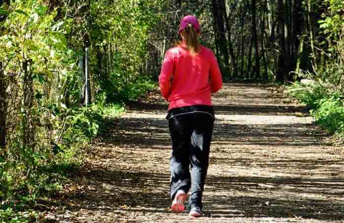 빨간색 점퍼를 입은 한 여자가 숲길에서 조깅을 하고 있는 모습