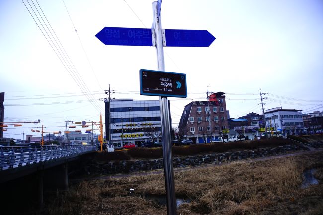 왼쪽에 넘어온 도장교&#44; 가운데 이정표&#44; 여주역 3.1km&#44; 뒤로는 개천&#44; 뒤로는 건물들&#44;