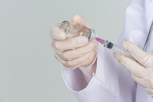 young-doctor-is-holding-hypodermic-syringe-with-vaccine-vial-rubber-gloves-gray-wall