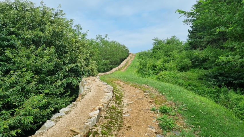 거의 직선으로 뻗은 좁은 토성길, 왼쪽엔 복원된 석축성벽, 푸른 하늘, 좌 우 울창한 숲,