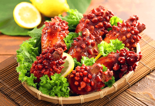 소쿠리에 통통한 멍게 7마리가 있고 멍게 아래에는 연두색 상추가 깔려있다. 그리고 레몬 조각 한 개가 있고 소쿠리 주변에도 레몬이 있다.