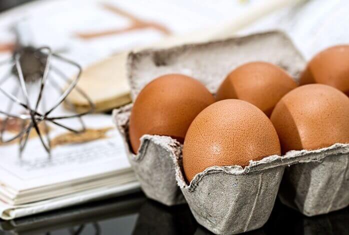 펼쳐진 노트 위에 거품기가 놓여져 있고 그 앞에 종이로 된 계란틀 안에 계란 5알이 들어있는 모습 