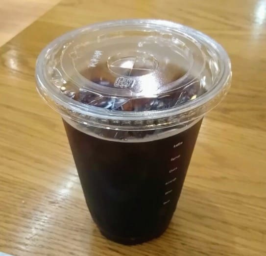 테이블 위에 커피가 플라스틱 일회용 컵에 담겨있다.