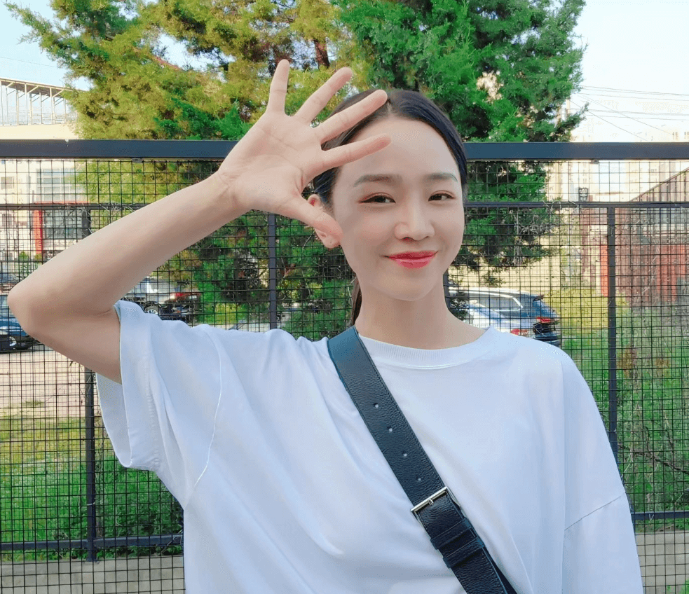 신혜선이 하얀색 반팔 티를 입고 검은색 크로스 가방을 어깨에 메고 한쪽 팔을 들어 얼굴 옆에 손가락 다섯개를 모두 펼쳐보이고 있다.