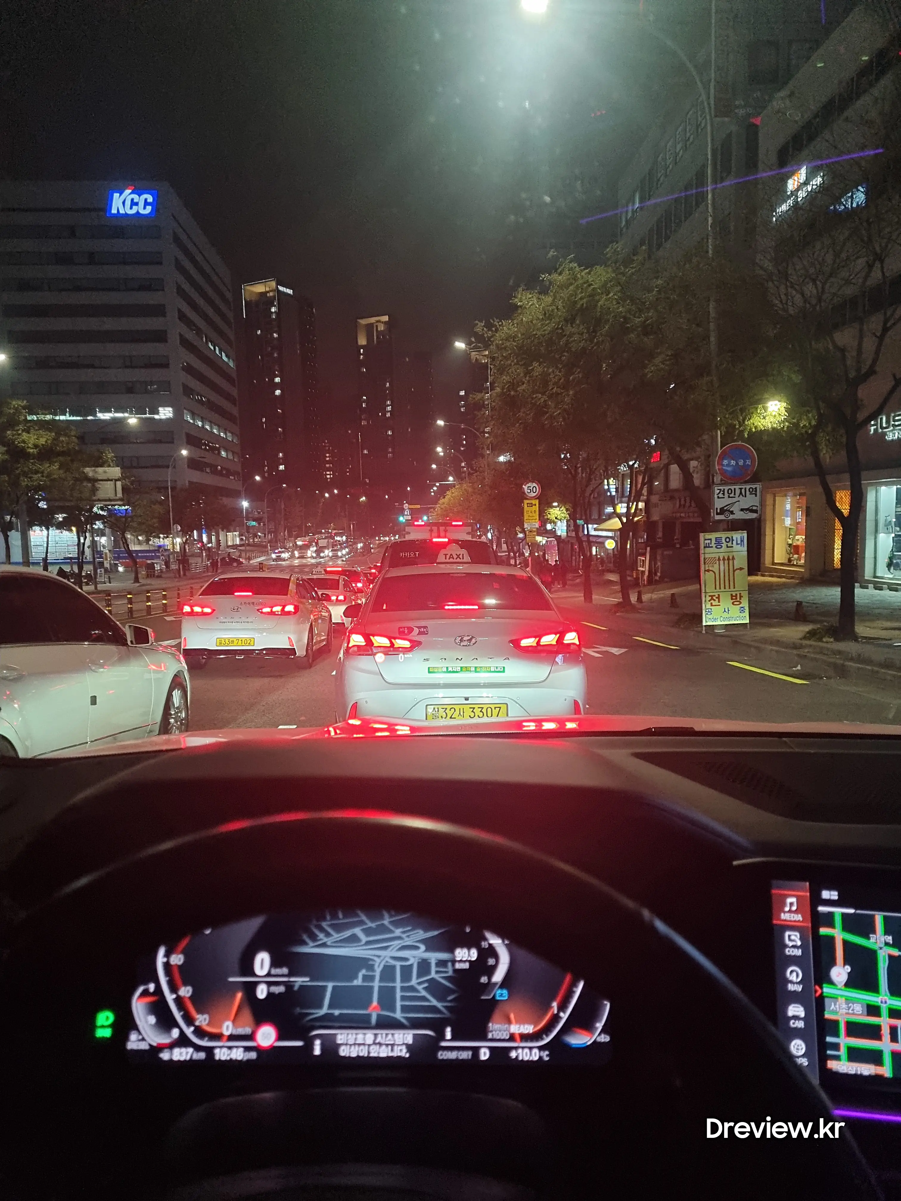 서울 시내의 밤거리를 달리고 있는 BMW 차량의 모습입니다. 차량의 계기판에는 "비상호출시스템에 이상이 있습니다."라는 문구가 표시되어 있습니다.