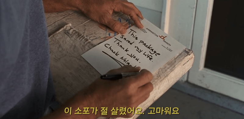 척이 4년 만에 고객에게 택배를 전달하기 전에 메모를 적는 스틸컷 '이 소포가 절 살렸어요, 고마워요.'라고 적고 있다