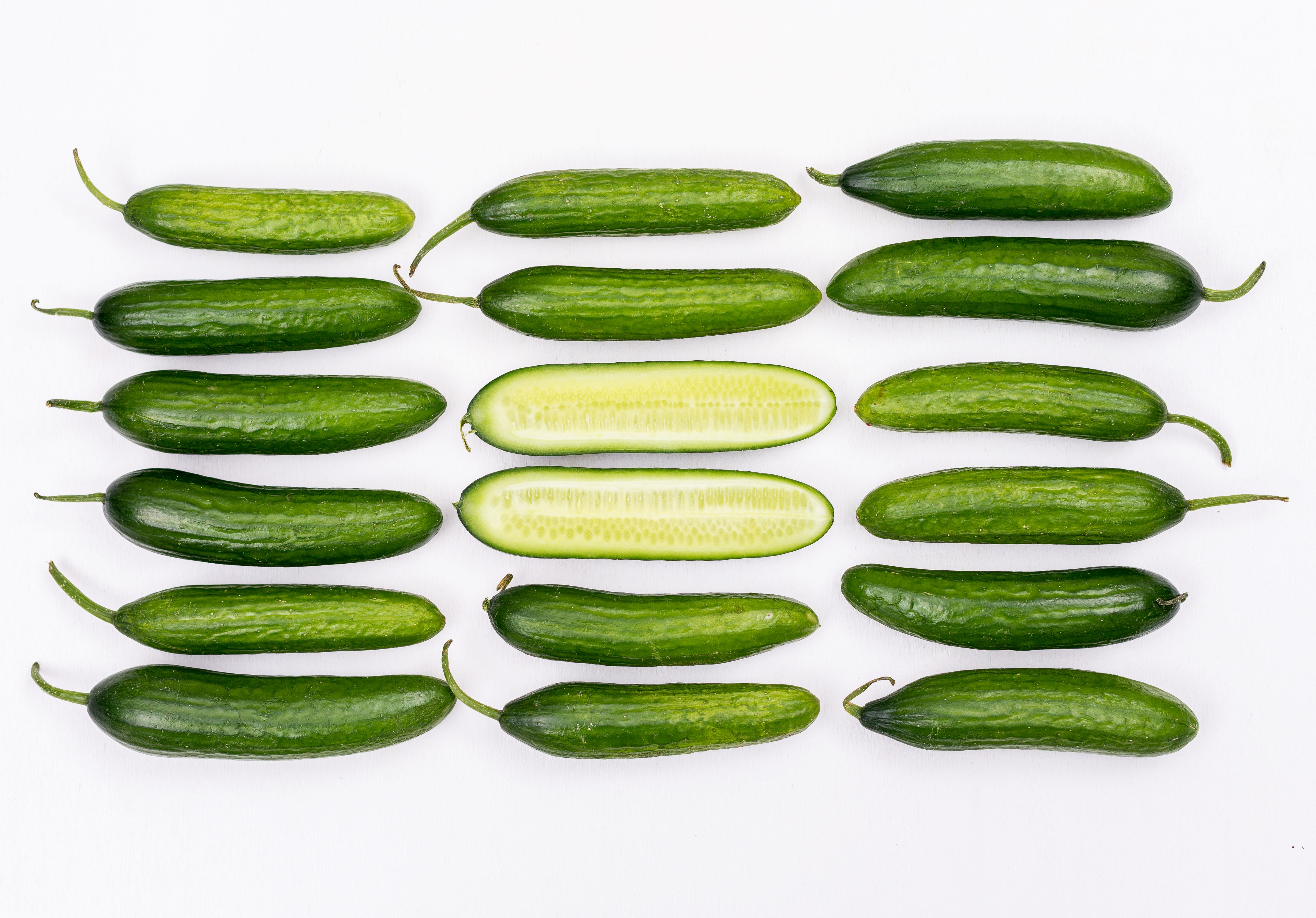 오이를 가지런하게 가로 3줄&#44; 세로 6줄로 한개씩 놓아두고 가운데 2개는 반으로 잘라 놓은 사진 (top-view-cucumber-sliced-middle-white-horizontal)