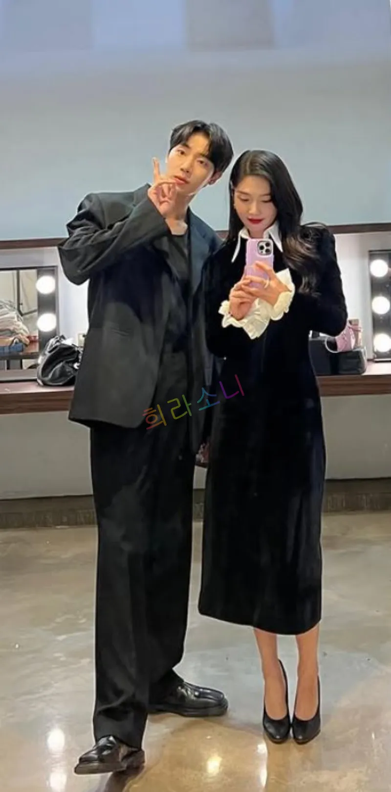 거울 앞에서 검은색 수트를 입은 추영우가 긴 검은 드레스를 입은 조이와 함께 서 있는 모습. 추영우는 한 손을 들고 브이(V) 포즈를 취하고 있으며&amp;#44; 조이는 핸드폰을 들고 셀카를 찍고 있다. 화려한 조명이 있는 드레싱룸이 배경이다.