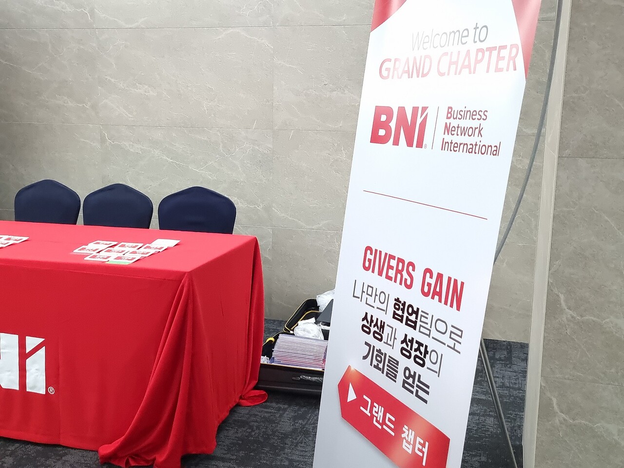 기버스게인 BNI 성남 그랜드 챕터 주간회의 런던홀 입구에 기버스게인 배너와 테이블위에 명찰 명함등이 있습니다.