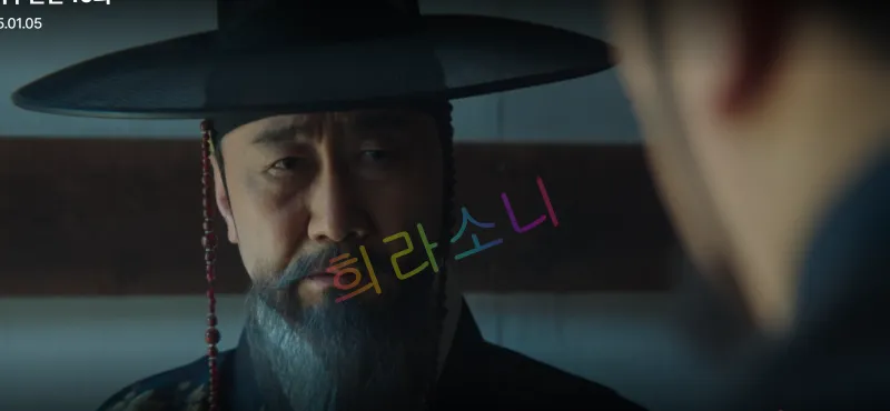검은 갓과 짙은 수염을 가진 박준기가 심각한 표정으로 지행수를 응시하고 있습니다. 
