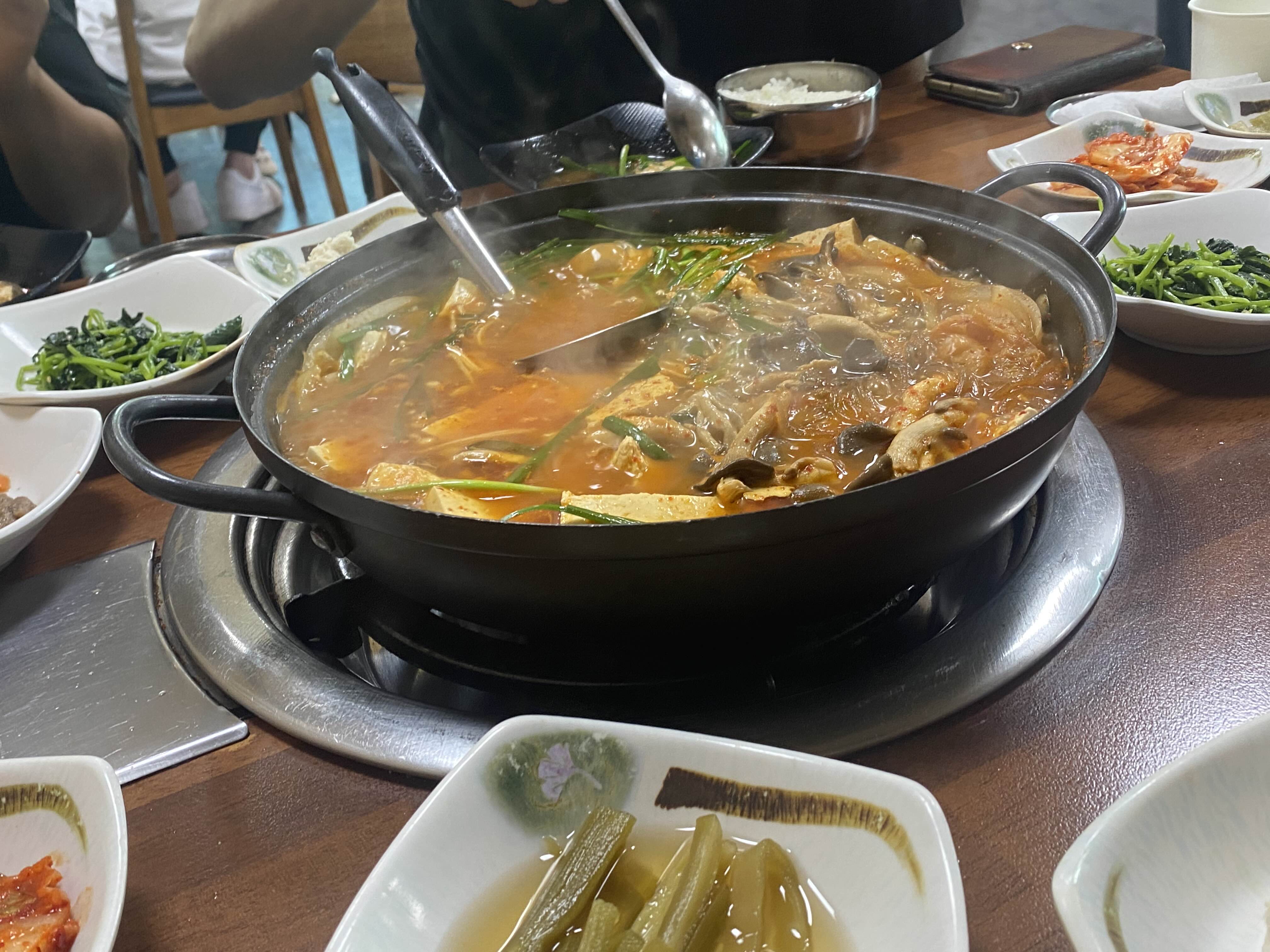 큰 검정색 솥 안에 들어있는 빨간 국물과 두부조각 및 버섯
