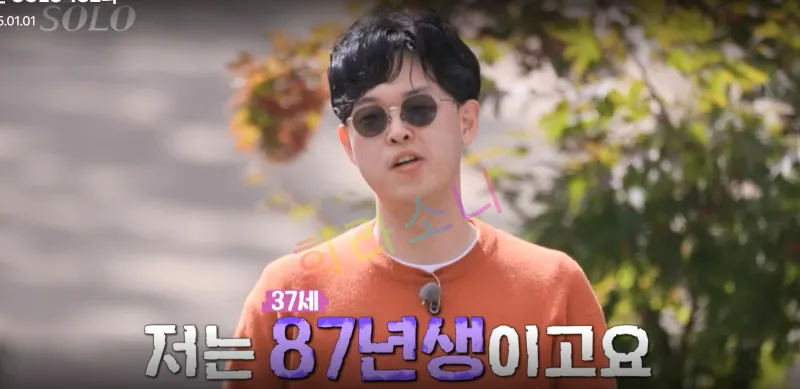 주황색 스웨터와 선글라스를 착용한 24기 영호가 밝은 야외에서 인터뷰를 진행하고 있다. 화면 하단에는 