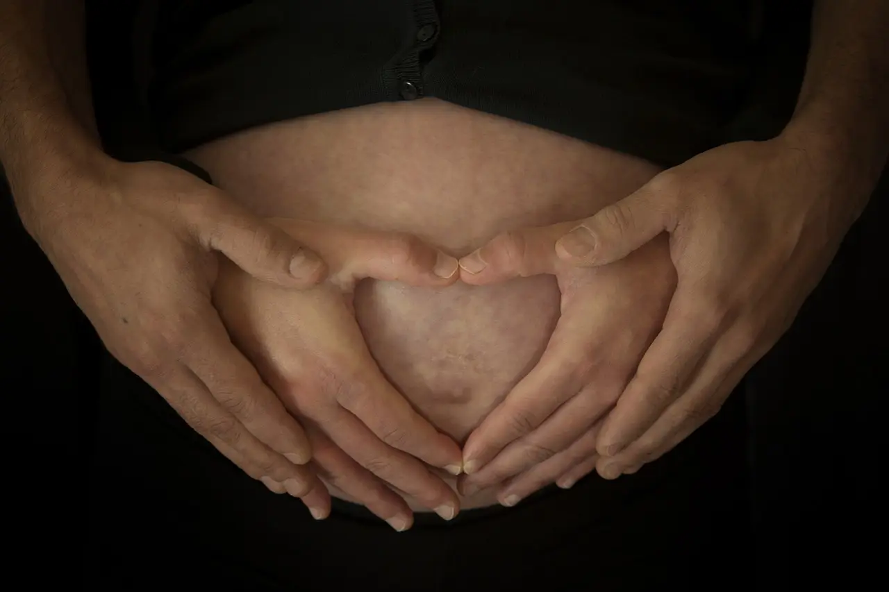 임신부 특례대출- 검은 옷을 입은 입신부 배꼽을 손으로 하트모양을 하여 감싸고 있는 여자손과 남자손