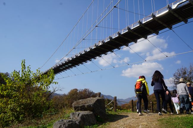 푸른 하늘&#44; 하늘 다리 밑 여성 1 오렌지색 배낭&#44; 여성 1 검은 옷&#44; 남성 1 회색 상의&#44; 남성 1 검은 옷&#44;