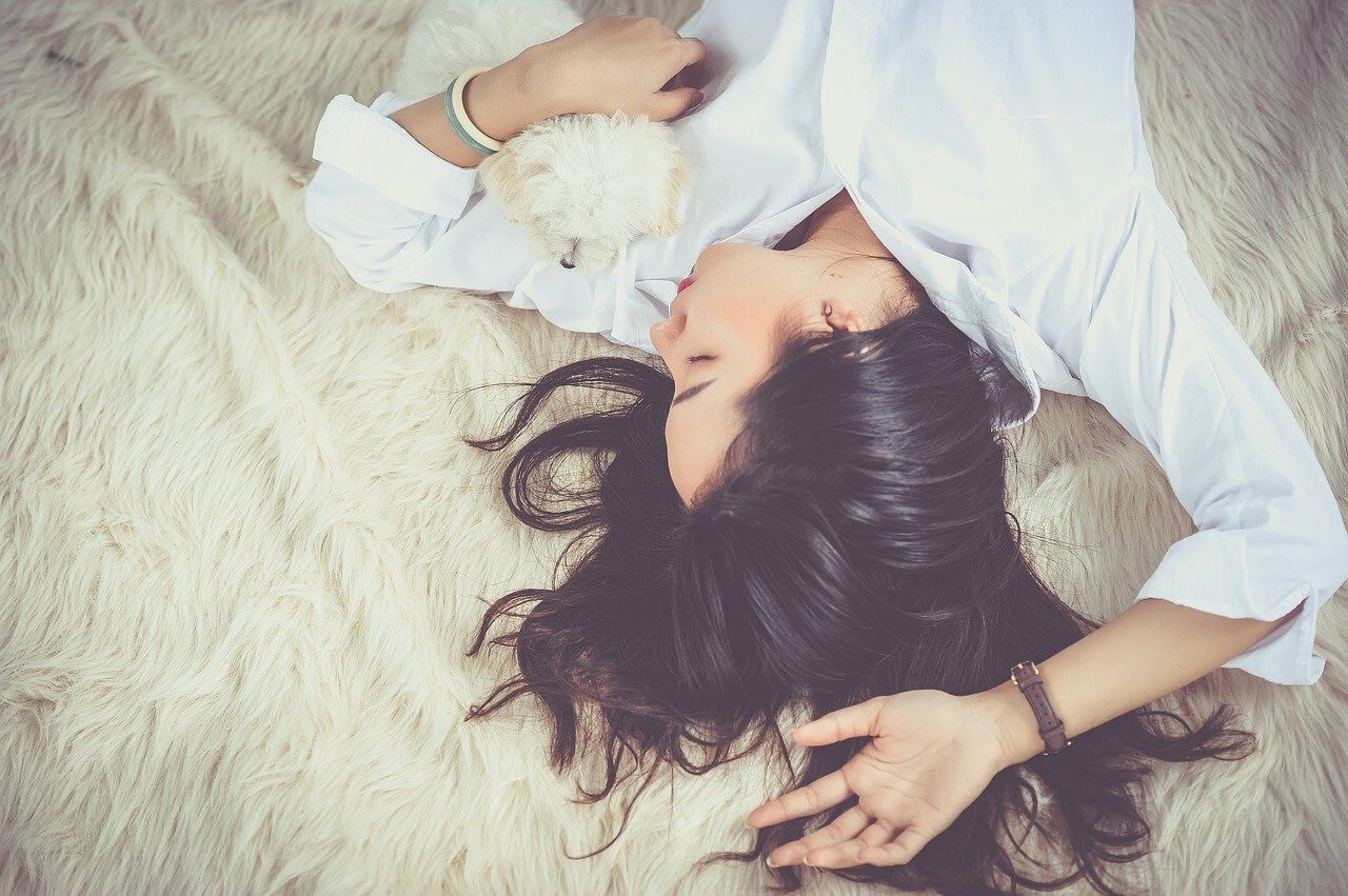하얀색 셔츠를 입고 털 침대에 누워서 잠을 청하고 있는 여성