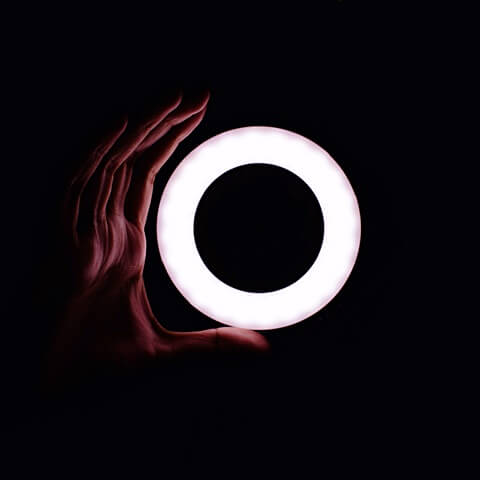 검은 배경 속에 도넛 모양의 동그란 전등에 불이 밝혀져 있고 그것을 손으로 감싸는 모양을 하고 있는 모습