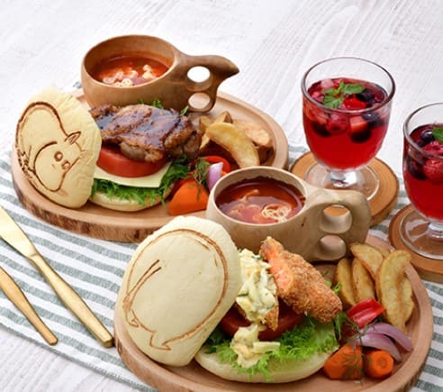 작은 나무 접시위에 햄버거와 스프 감자튀김 등등이 올려져 있고 햄버거 위에는 캐릭터 모양이 찍혀 있다.