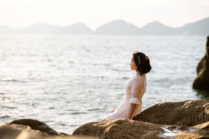 바닷가 바위 앞에 앉아있는 여성 사진