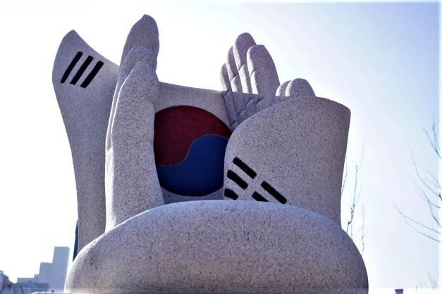 두 손을 감싼 태극기 대라석 조형물 클로즈 업&#44; 로 앵글&#44; 눈부신 흐린 하늘&#44;