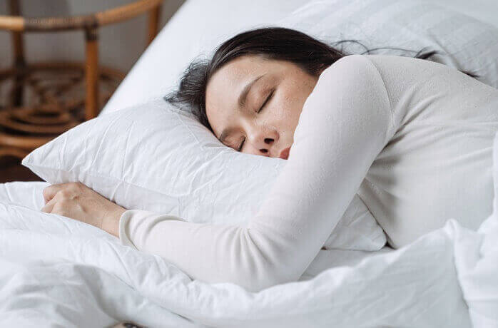 하얀색 침구류에서 흰 옷을 입은 한 여자가 자고 있는 모습