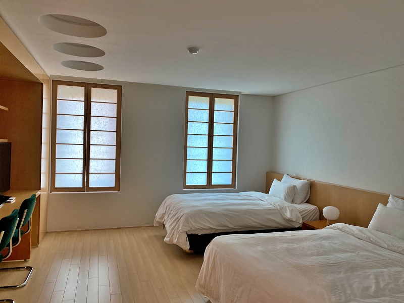 흰벽지로된 방에 침대2개가 놓여있고 나무창틀로된 2개창문이 있다