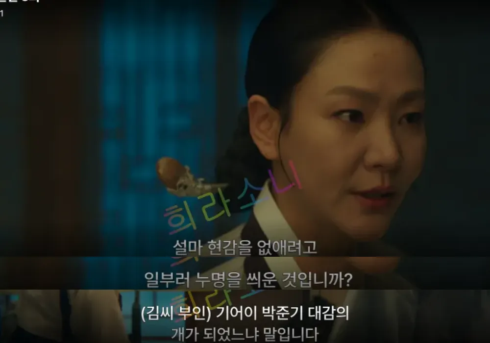 단정한 흰색과 남색 한복을 입은 김씨 부인이 진지한 표정으로 대화하는 장면. 머리는 단아하게 올려 묶었으며&amp;#44; 화면 하단 자막에는 &amp;quot;(김씨 부인) 기어이 박준기 대감의 개가 되었느냐 말입니다&amp;quot;라는 문구가 적혀 있다.