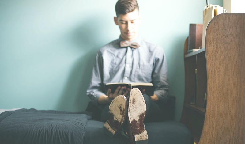 A male international student reading a document in a dorm room, preparing for U.S. tax filing