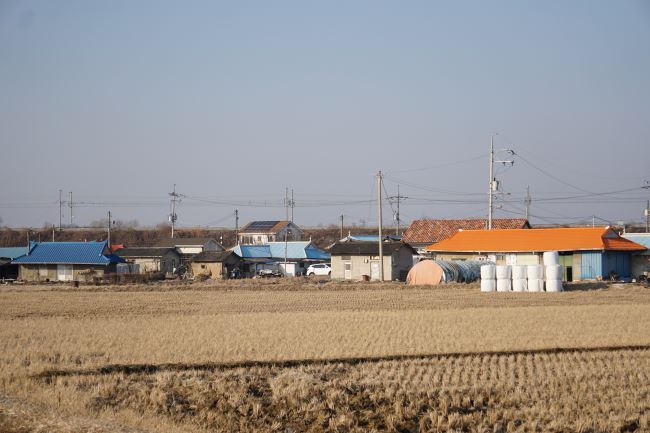 들판 뒤로 보이는 마을 풍경&#44; 왼쪽에 파란 지붕&#44; 우측에 오렌지색 지붕&#44; 흐린 하늘&#44;