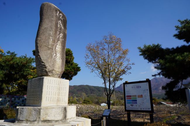 수복기념 표지석&#44; 검은 돌에 흰글씨&#44; 한자&#44; 맡받침은 사각 육면체 대리석&#44; 옆에는 경흥길 안내판&#44; 푸른 하늘&#44; 뒤로는 나무 세 그루&#44;