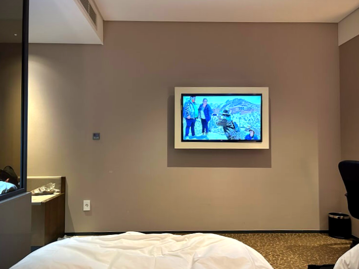 베이지-벽면에-TV가-걸려있는-호텔-객실-내부를-찍은-사진