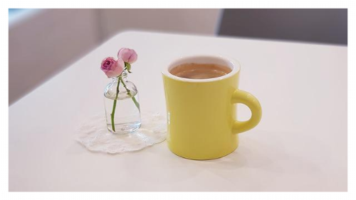 투명 유리병에 분홍색 꽃 두송이 옆 노란색 커피 컵