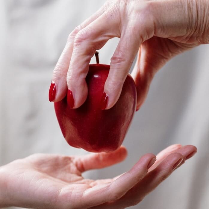 나이든 여자 손에서 젊은 여자 손으로 빨간 사과가 건네지는 모습